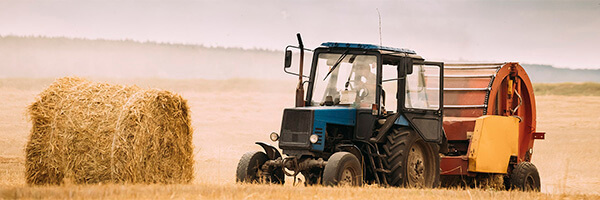 Seguros Agrarios - Tractor azul en el campo recogiendo paja para dar de comer al ganado Seguros Agrarios - Tractor azul en el campo recogiendo paja para dar de comer al ganado