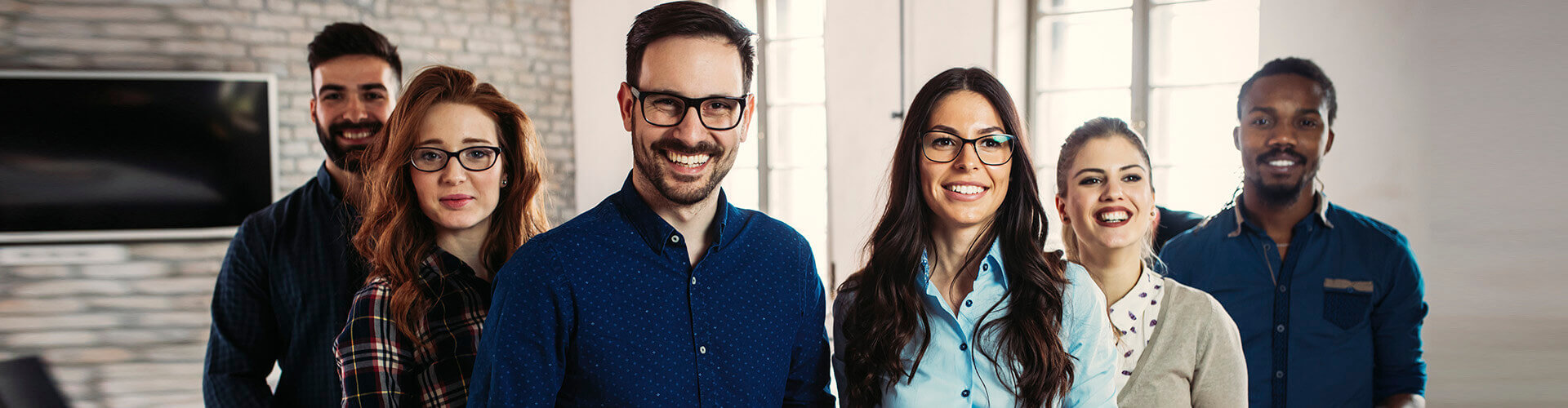 Programa Porque Somos Asi - Grupo de personas en fila sonriendo unas al lado de otras en la oficina Programa Porque Somos Asi - Grupo de personas en fila sonriendo unas al lado de otras en la oficina