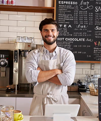 Autonomoentzako Promueve Programa ezagutzen duzu?- Dueño joven de una cafeteria con delantal y los brazos cruzados sonriendo tras la barra Autonomoentzako Promueve Programa ezagutzen duzu?- Dueño joven de una cafeteria con delantal y los brazos cruzados sonriendo tras la barra