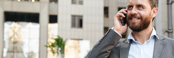 Seguros Banca Privada - Hombre de negocios con un traje gris y camisa blanca hablando por el móvil junto a un edificio en una ciudad Seguros Banca Privada - Hombre de negocios con un traje gris y camisa blanca hablando por el móvil junto a un edificio en una ciudad