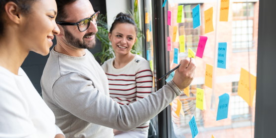 Guía Práctica para Emprender - Mujeres y hombre pensando en oficina señalando post it en cristal - [dm:entidad]