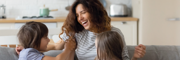 Madre y dos hijos riendo en el sofá de casa