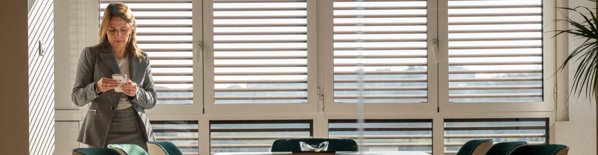 Ruralvía Broker - Mujer de negocios de pie con su móvil en la oficina Ruralvía Broker - Mujer de negocios de pie con su móvil en la oficina