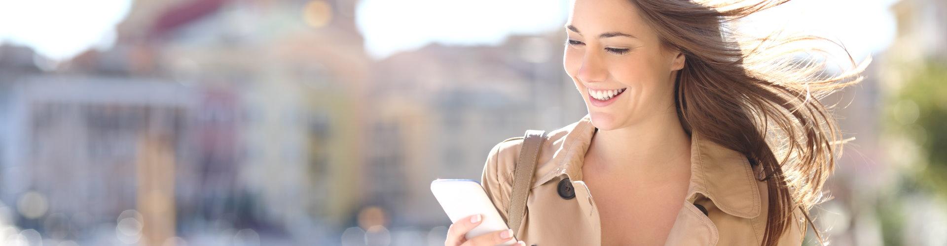 Mujer joven sonriendo mirando al móvil en la calle