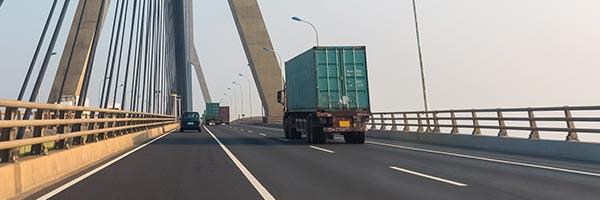 Seguro de Transportes - Carretera de una ciudad donde circulan camiones de transporte de mercancias junto a un puente Seguro de Transportes - Carretera de una ciudad donde circulan camiones de transporte de mercancias junto a un puente