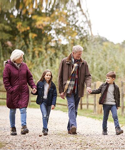 Préstamo Pensión - Ventajas Ventajas-particulares-abuelos-nietos-caminando-sonriendo-campo-rodeados-arboles